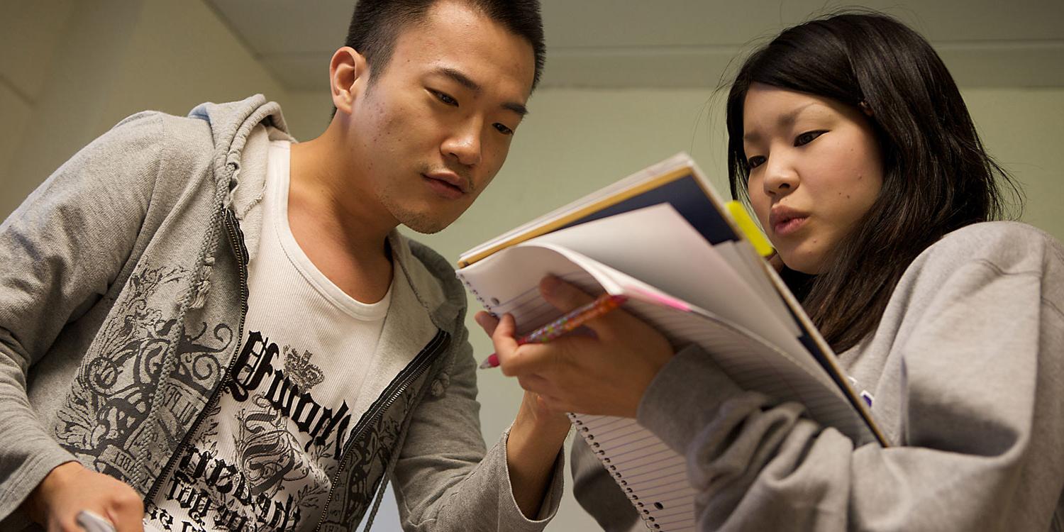 young man helping young woman holding a 不ebook 和 pen